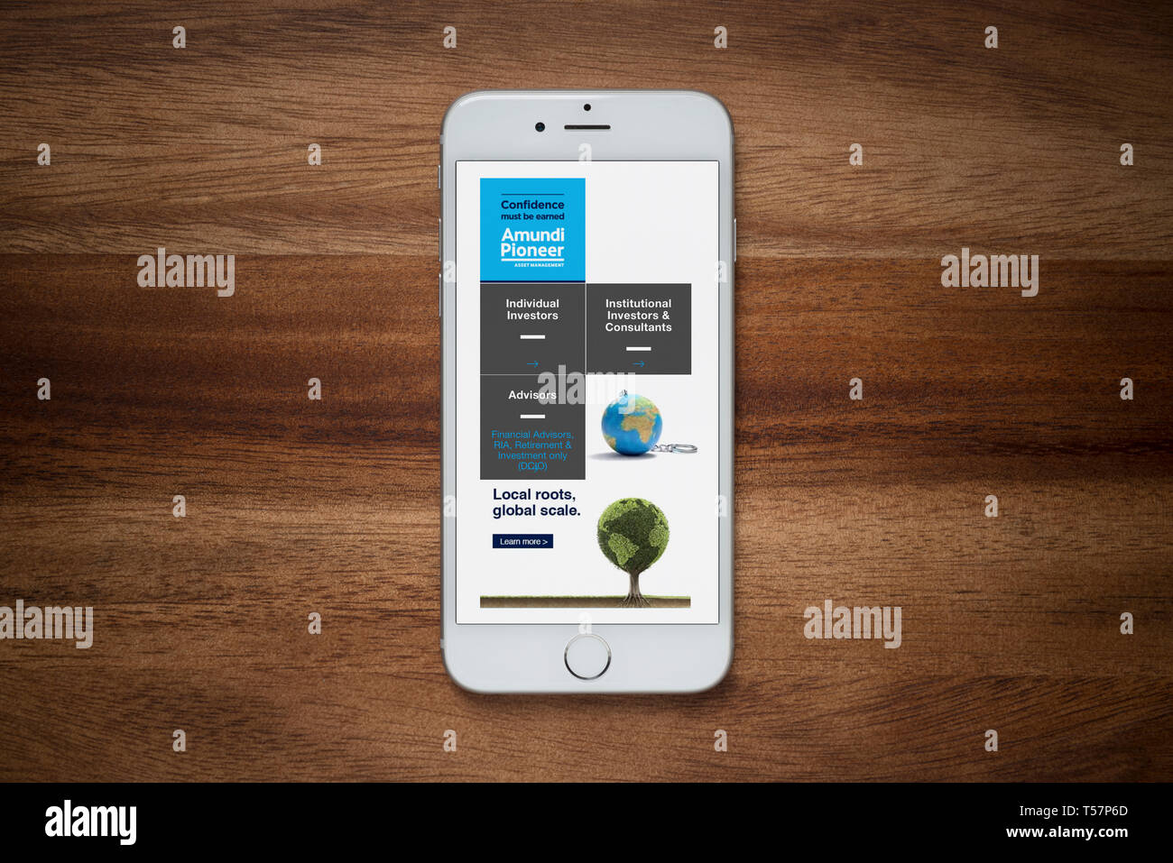 An iPhone showing the Amundi Asset Management website rests on a plain wooden table (Editorial use only). Stock Photo