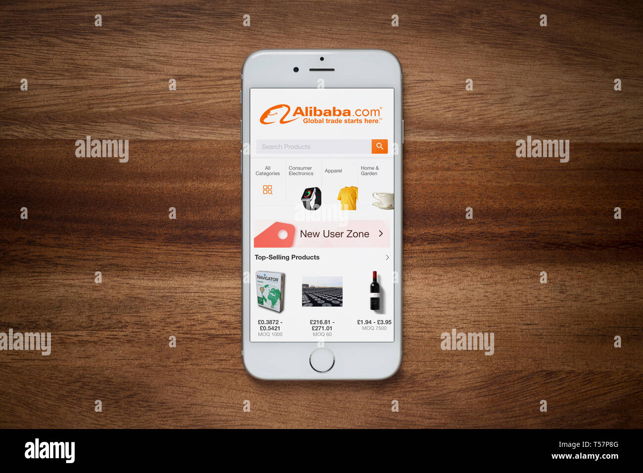 An iPhone showing the Alibaba website rests on a plain wooden table (Editorial use only). Stock Photo