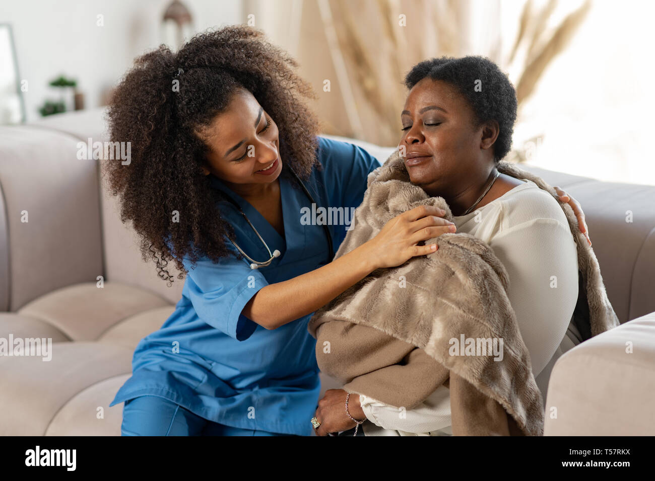 Caring curly nurse giving warm plaid to patient after catching cold