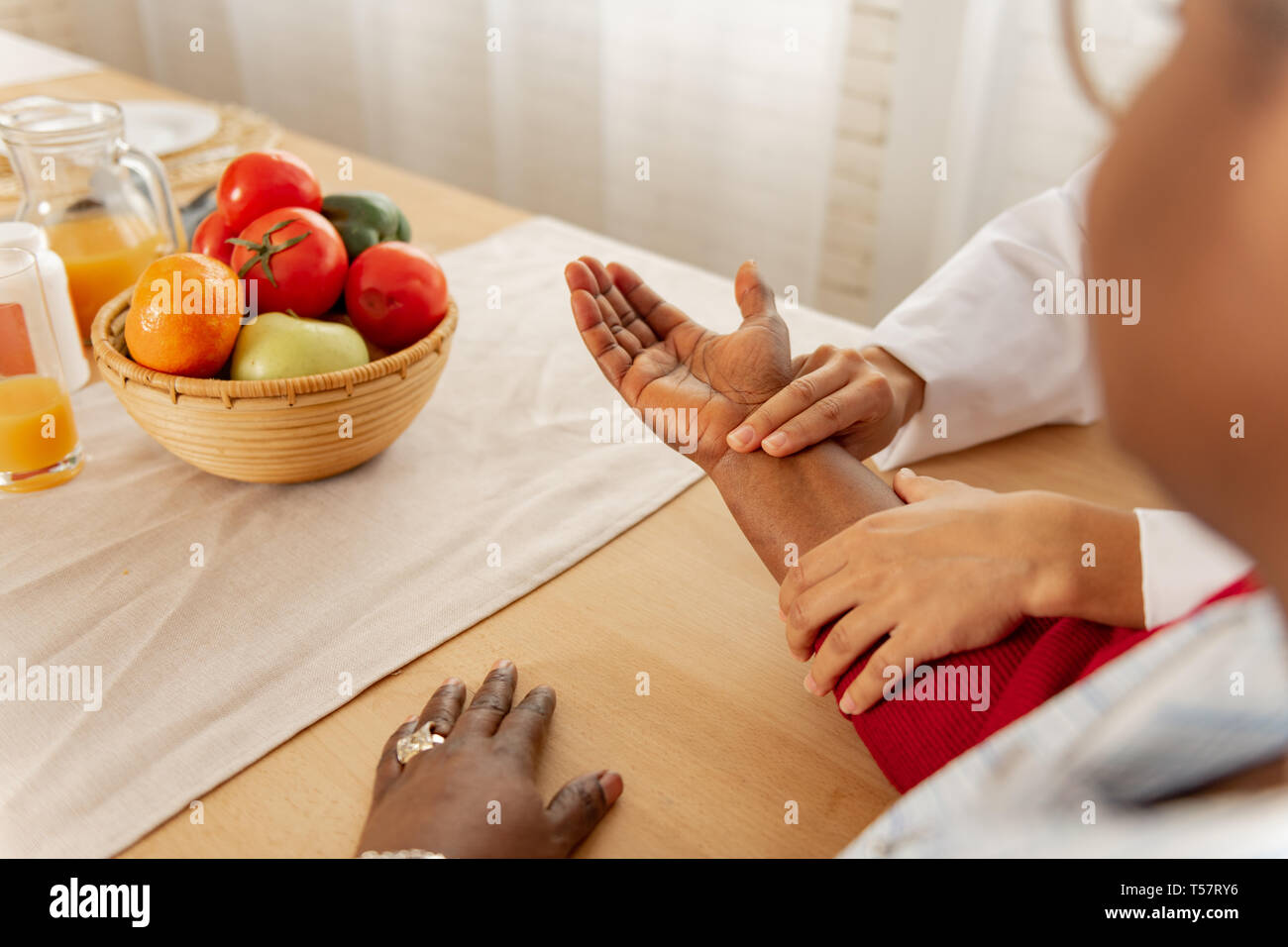 Nurse in white jacket putting two fingers on wrist of the patient Stock