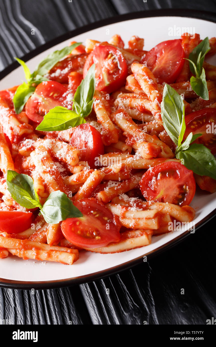 Delicious Italian pasta Casarecce with tomato sauce, parmesan and basil closeup on a plate on the table. Vertical Stock Photo