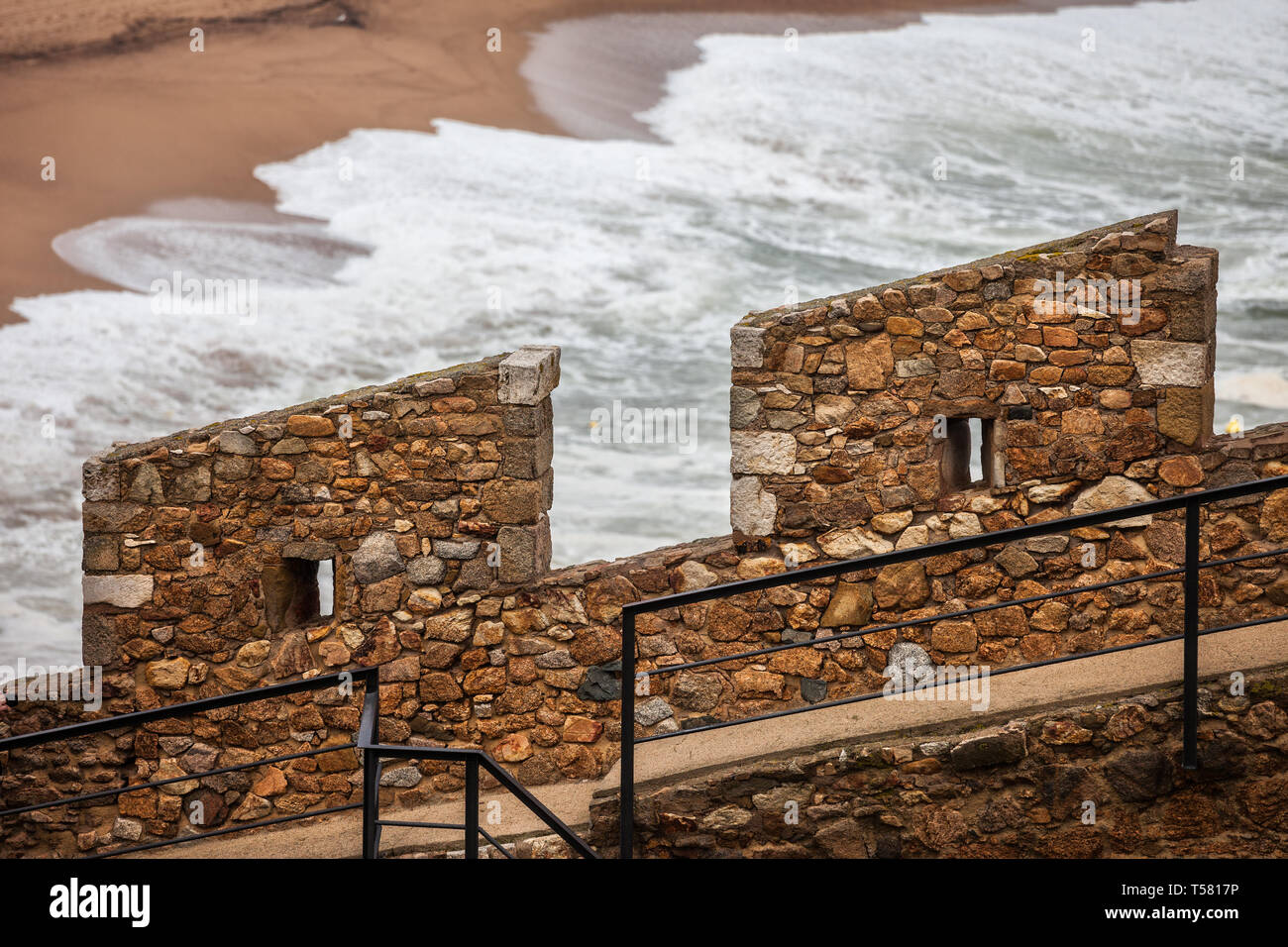 Defensive medieval stone wall battlement with two merlons and embrasures by the sea, old city wall fortification in Tossa de Mar, Catalonia, Spain Stock Photo