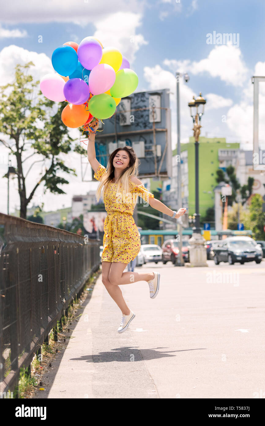 A happy girl jumps with a lot of ballons in her hands. Stock Photo