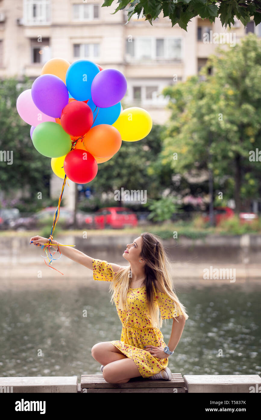 Happy girl are sitting down and are looking to her ballons. Stock Photo