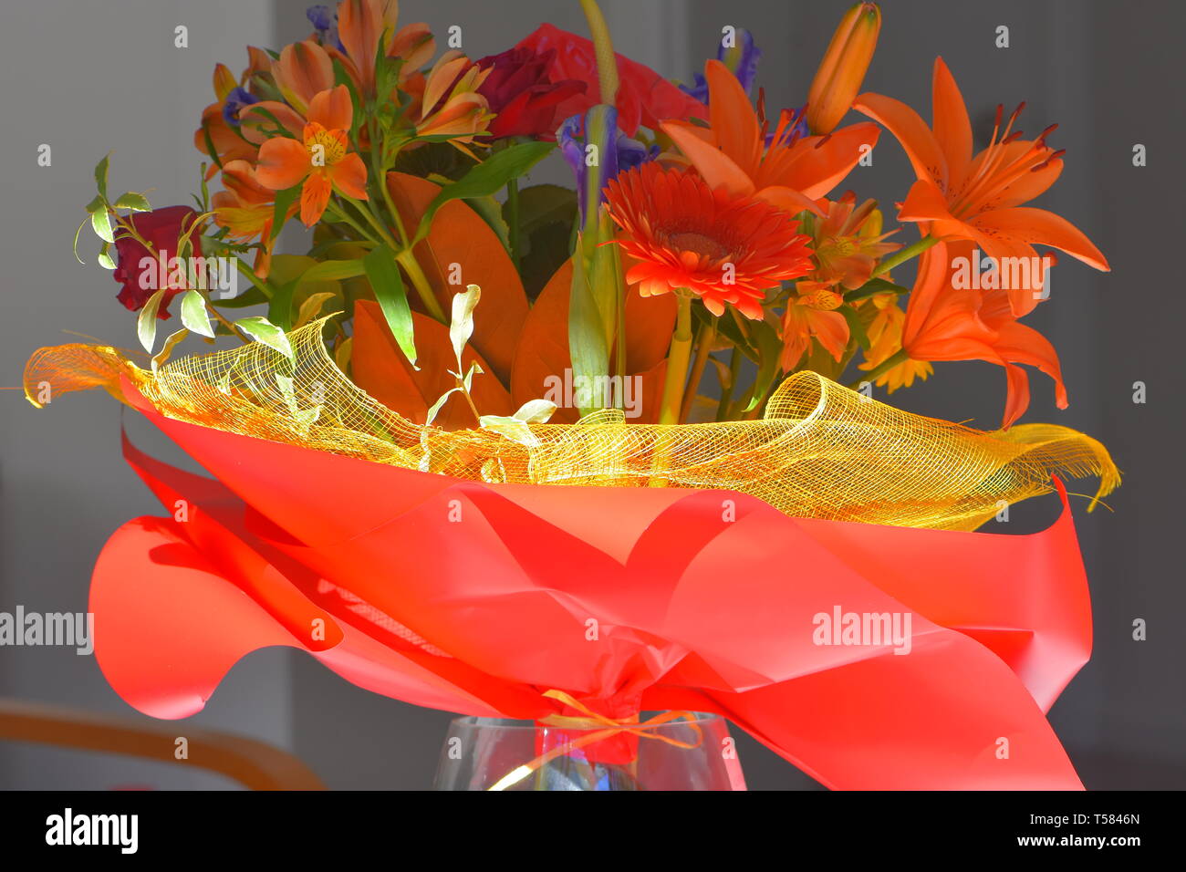 Colorful bouquet of various flowers in yellow mesh and red paper on gray background. Stock Photo