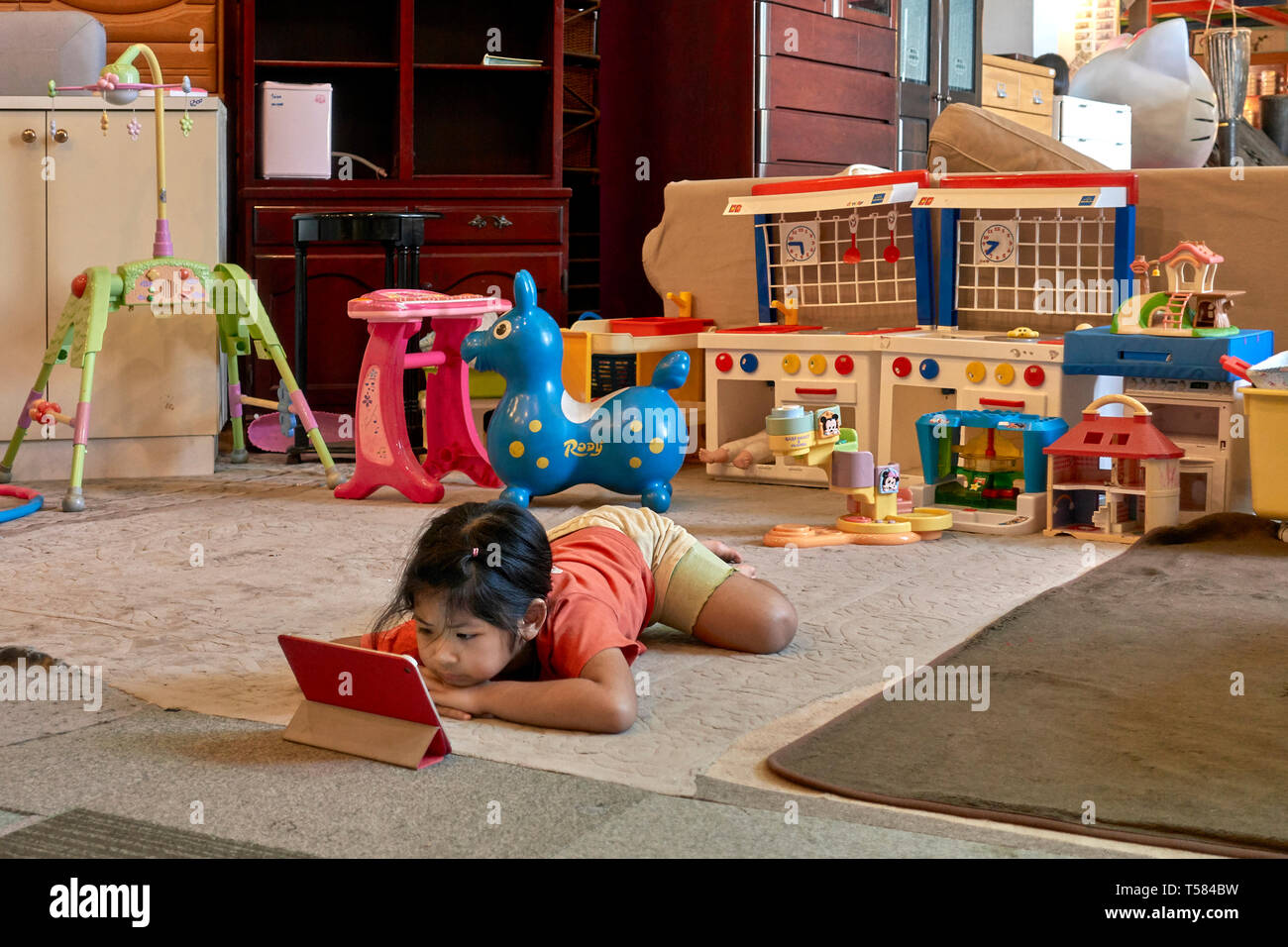 child with Ipad. Young girl engrossed with her modern Ipad and ignoring her traditional toys. Concept of old v new. Stock Photo