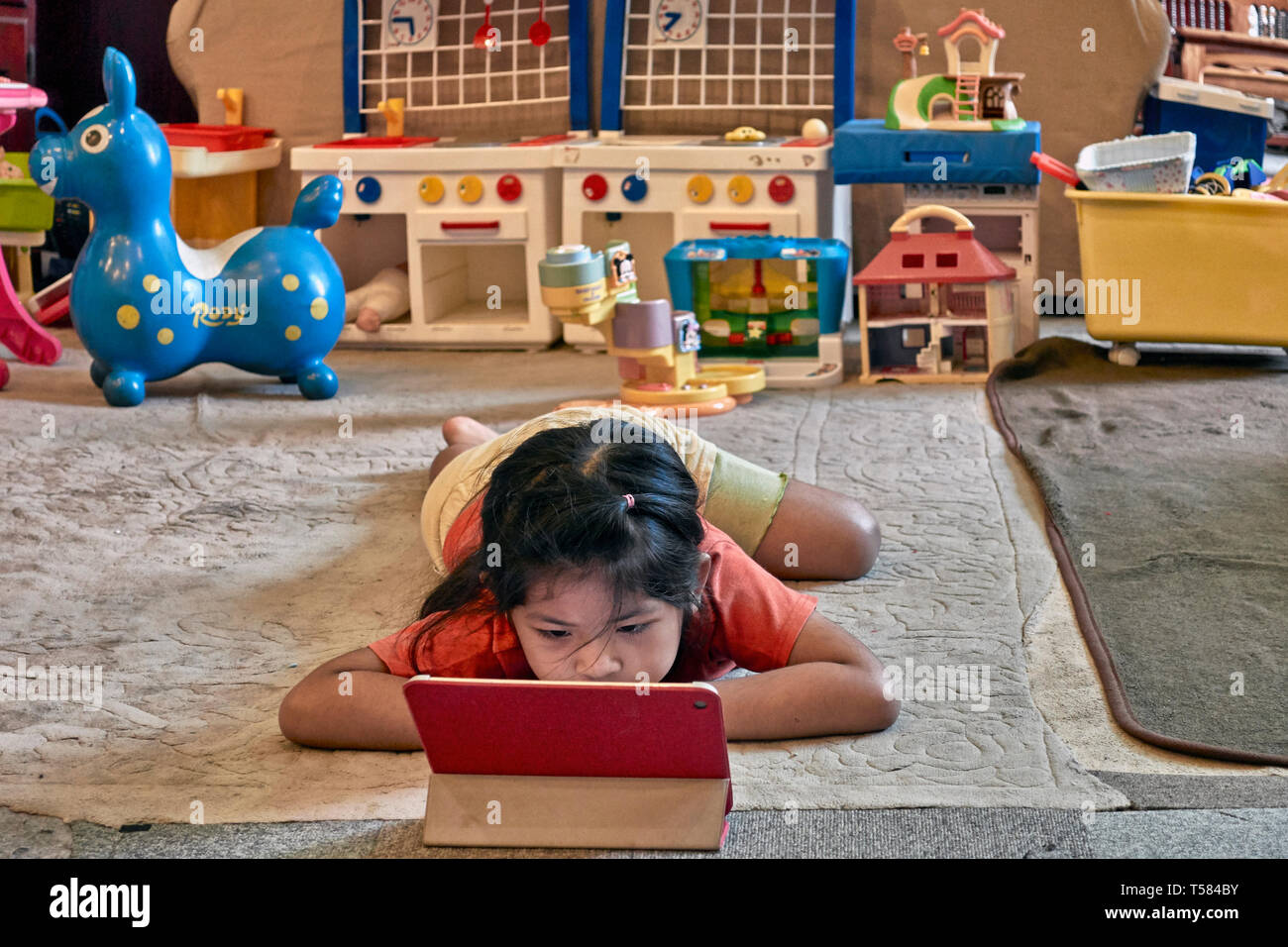 child with Ipad. Young girl engrossed with her modern Ipad and ignoring her traditional toys. Concept of old v new. Stock Photo