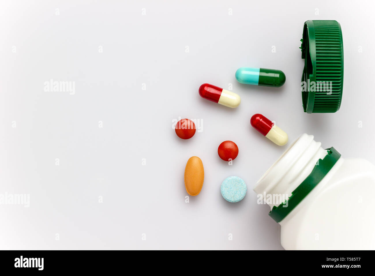 Multicoloured capsules with white medicine bottles and green caps on white background. Copy space for text or articles. Concepts of health and medicin Stock Photo