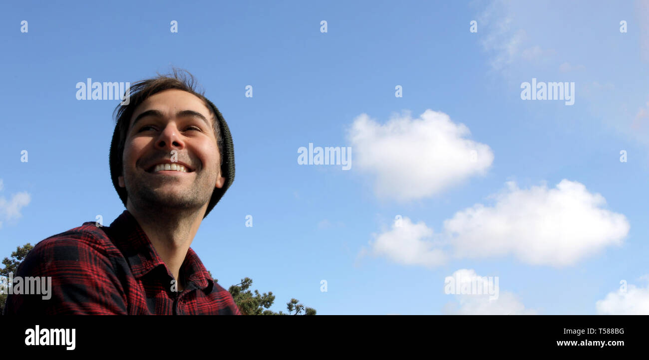 Portrait of an authentic and genuine hipster man smiling on a blue sky with white clouds background. Stock Photo