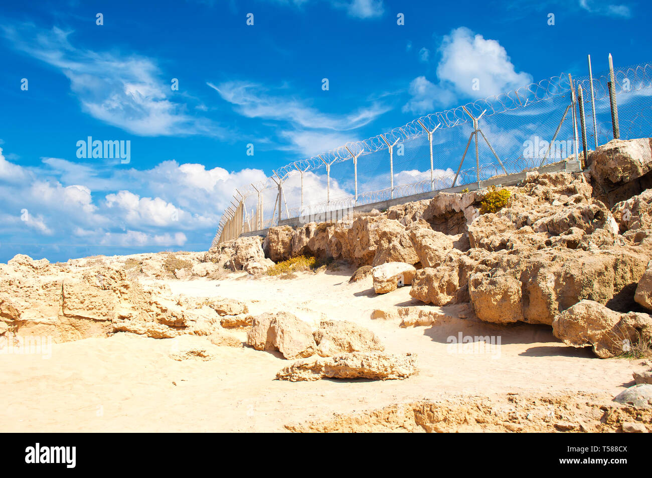 Military fence from barbed wire on a barren terrain with many rock ...