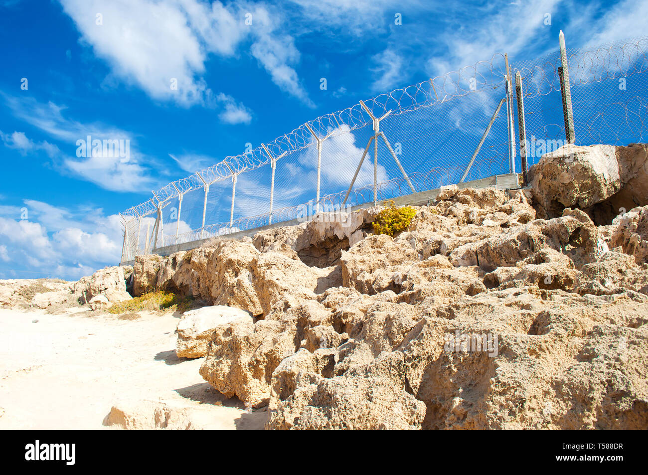 Military fence from barbed wire on a barren terrain with many rock ...