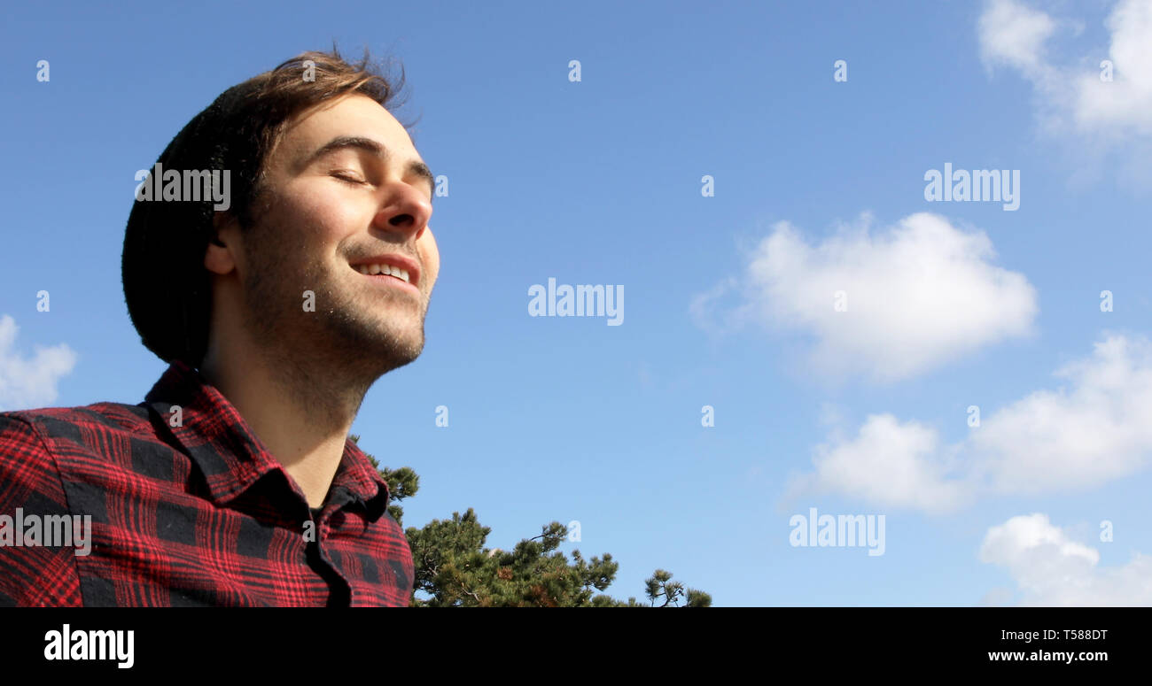 Portrait of an authentic and genuine hipster man smiling on a blue sky with white clouds background. Stock Photo