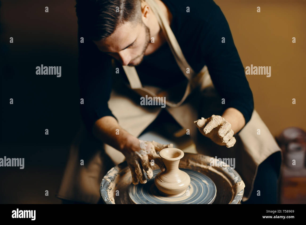 Man potter working on potters wheel making ceramic pot from clay in ...