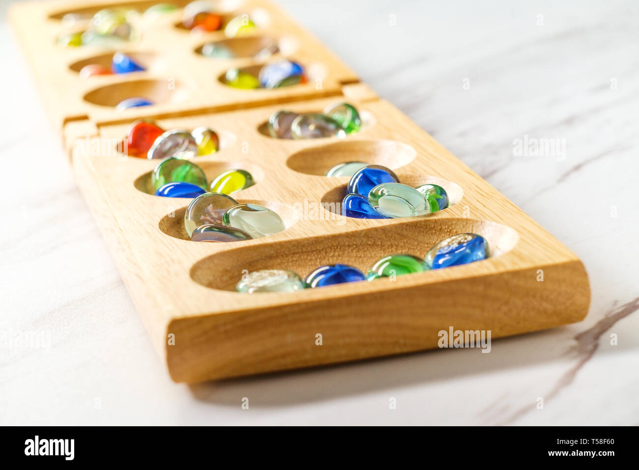 Traditional Mancala boardgame with glass pieces on marble table Stock
