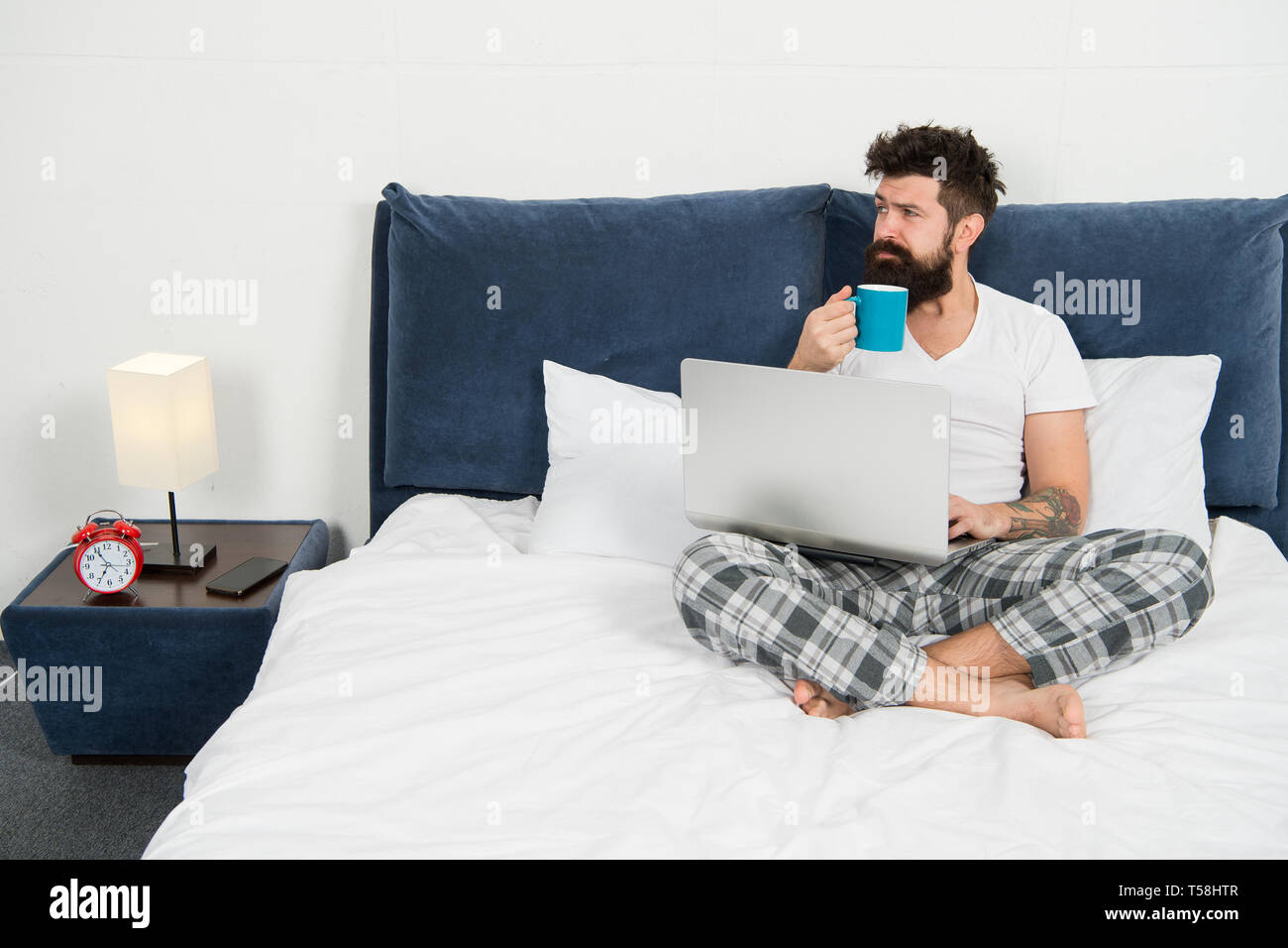 Hipster bearded guy pajamas freelance worker. Remote work concept. Social networks internet addiction. Online shopping. Man surfing internet or work online. Just woke up and already at work. Stock Photo