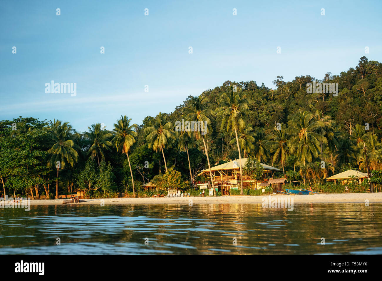 Port Barton, Palawan, Philippines - February 2, 2019: People on tropical beach with trees against wooden hotel at sunset Stock Photo