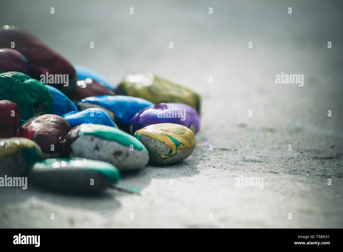 Many small pebbles covered with multicolored paint lie on the surface close-up Stock Photo