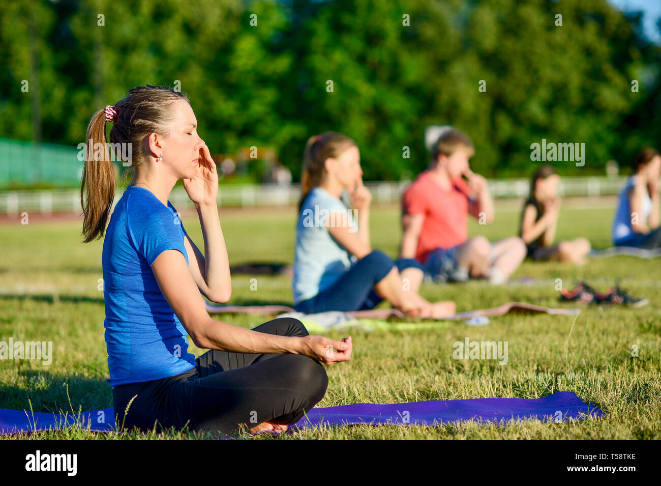 Young woman in a blue shirt doing yoga in a group at the city stadium, Russia, Kursk region, Zheleznogorsk, June 2018. The concept of a healthy lifest Stock Photo