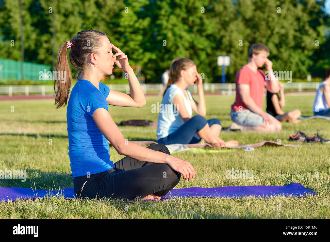 Young woman in a blue shirt doing yoga in a group at the city stadium, Russia, Kursk region, Zheleznogorsk, June 2018. The concept of a healthy lifest Stock Photo
