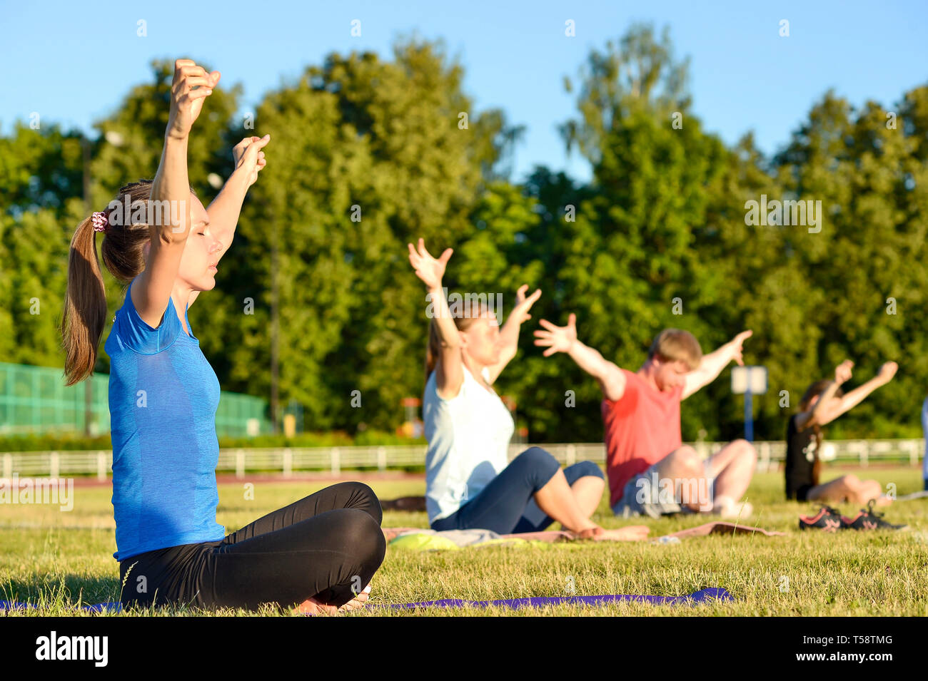 Yoga exercises class breathing technique group of people at the city stadium Russia, Kursk region, Zheleznogorsk, June 2018. A young woman in the fore Stock Photo