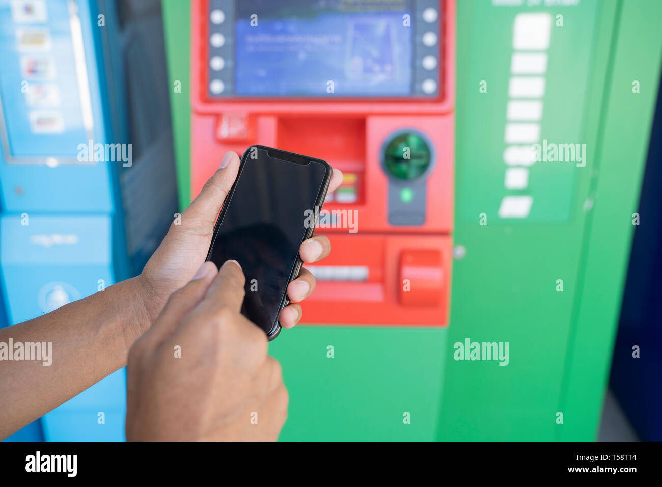 Man holding mobile phone with black screen at an ATM. Security code on an Automated Teller Machine - Image Stock Photo