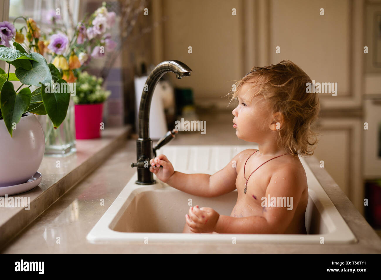 Baby taking bath in kitchen sink. Child playing with foam and soap