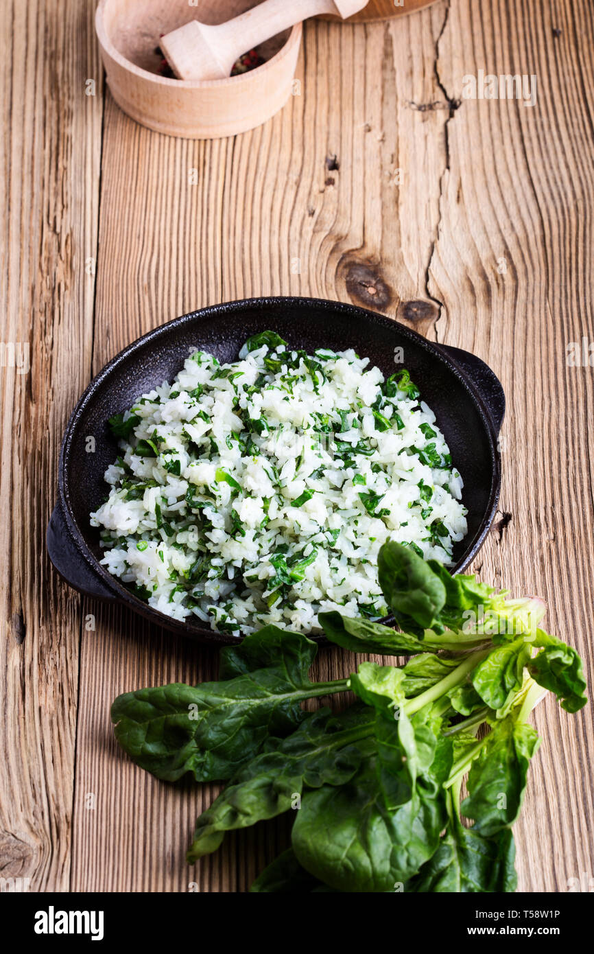 White rice with spinach served in cast iron skillet on rustic wooden table with fresh green leaf vegetables, plant based meal, close up, selective foc Stock Photo