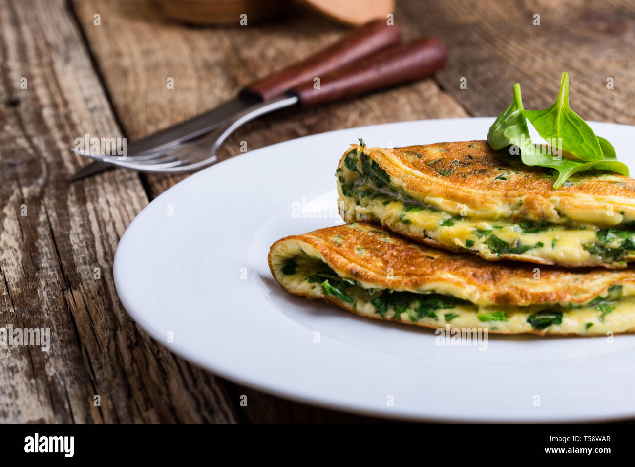 Baby spinach and parmesan cheese omelette, healthy vegetarian breakfast or brunch on wooden rustic table, close up, selective focus Stock Photo