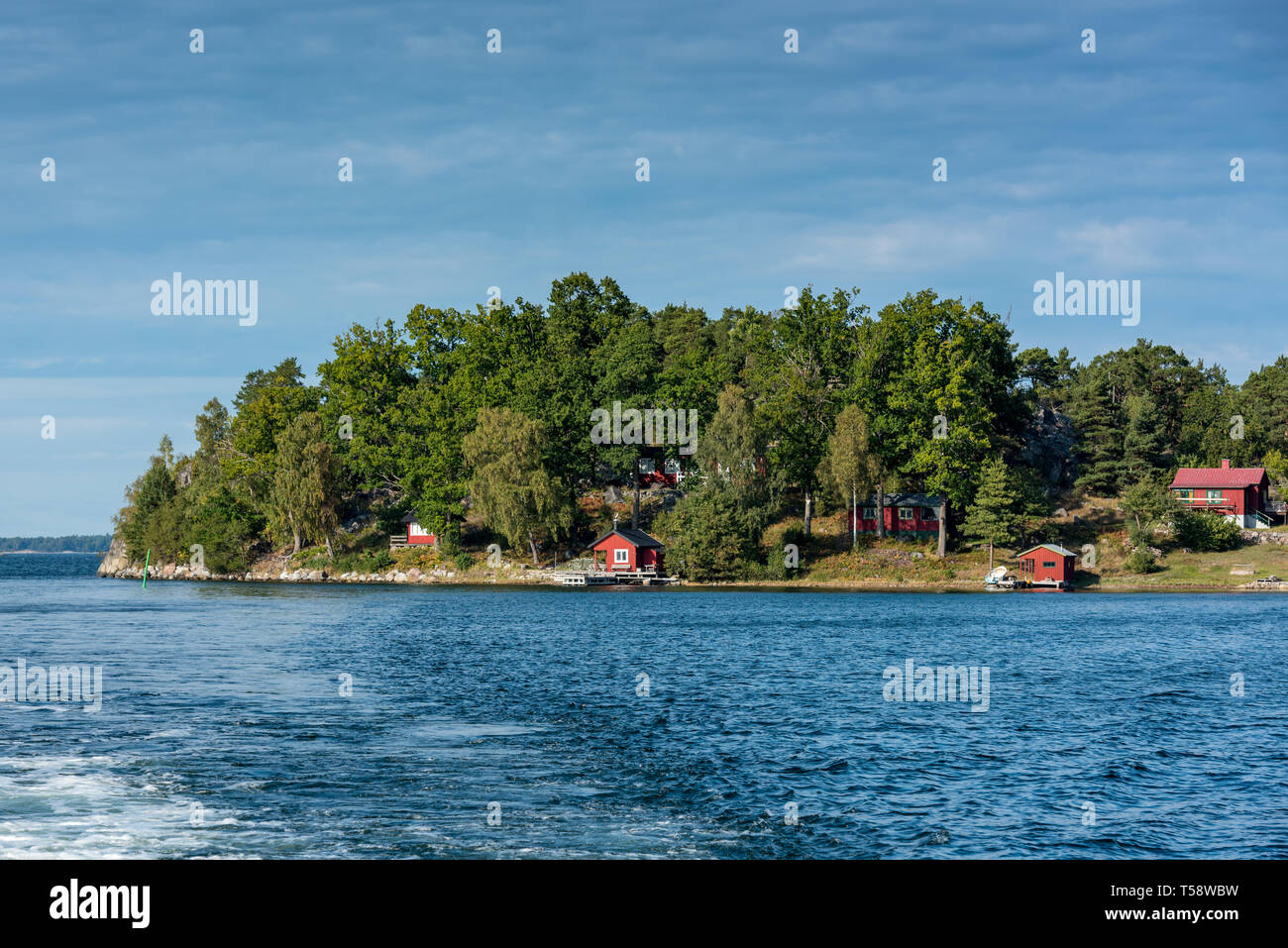 Traditional small red fishermen's cottages and holiday homes line the waterfront of a small islet in the Stockholm archipelago Stock Photo