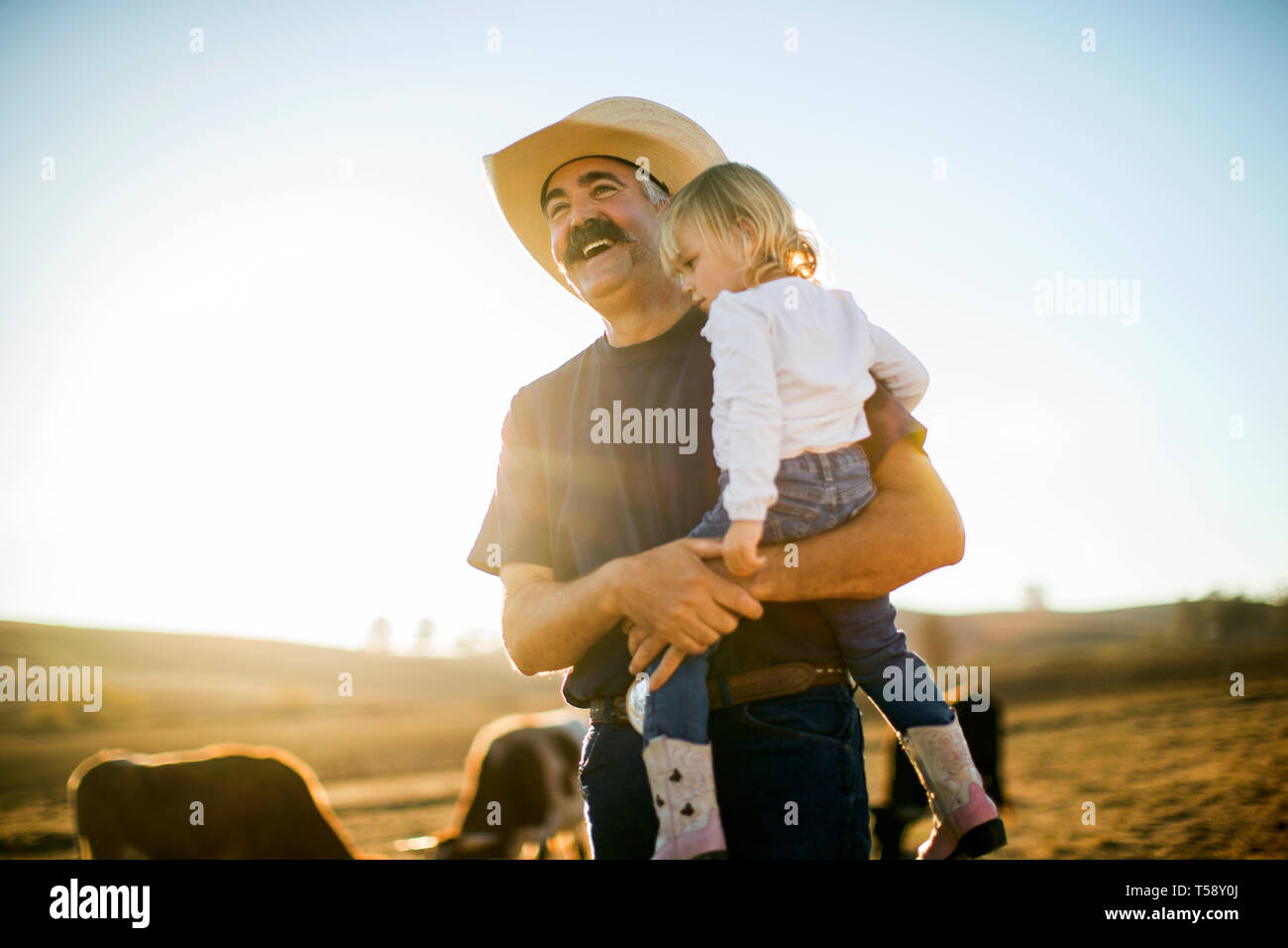 Cowboy rancher holding his toddler daughter in his arms while they are out on the ranch. Stock Photo
