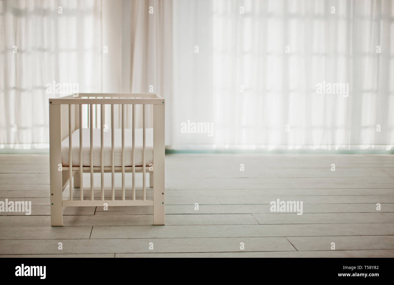 Empty white crib in a white room waiting for a baby. Stock Photo
