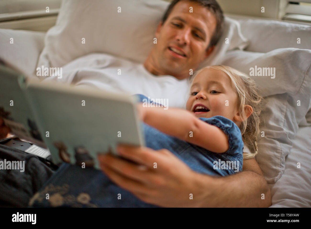 Father lying down reading a book with his daughter. Stock Photo