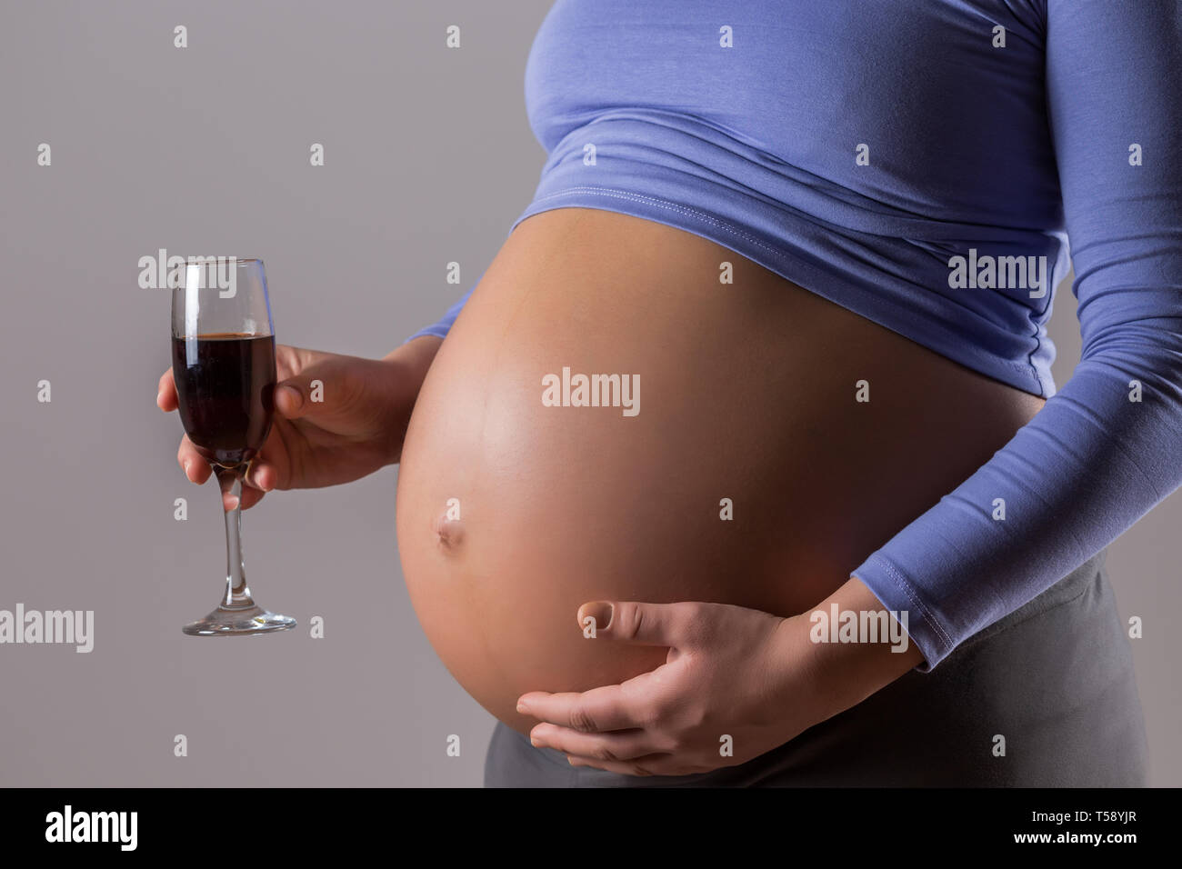 Image of pregnant woman drinking wine on gray background. Stock Photo