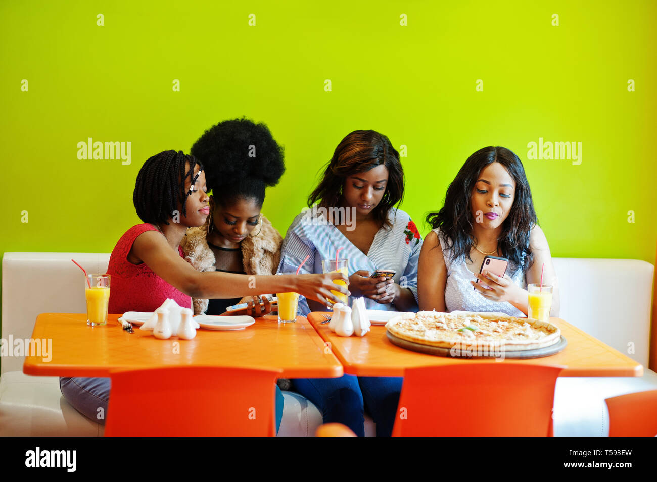 Four young african girls in bright colored fast food restaurant making  photo of pizza in their mobile phones Stock Photo - Alamy