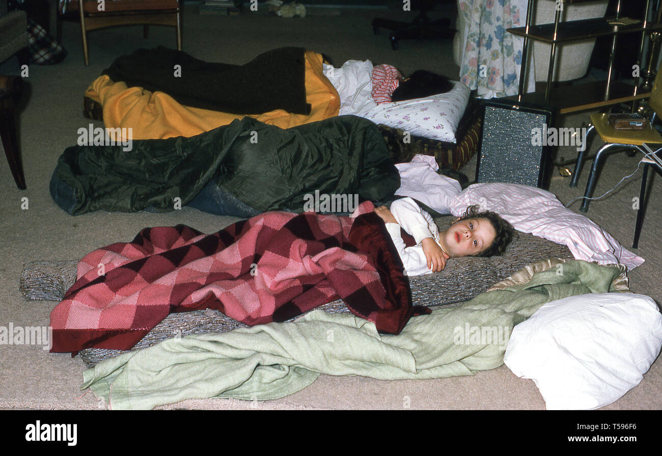 1970s, historical, three young children lying on airbeds and blankets in the middle of a carpeted floor, with one youngster in a green sleeping bag Stock Photo