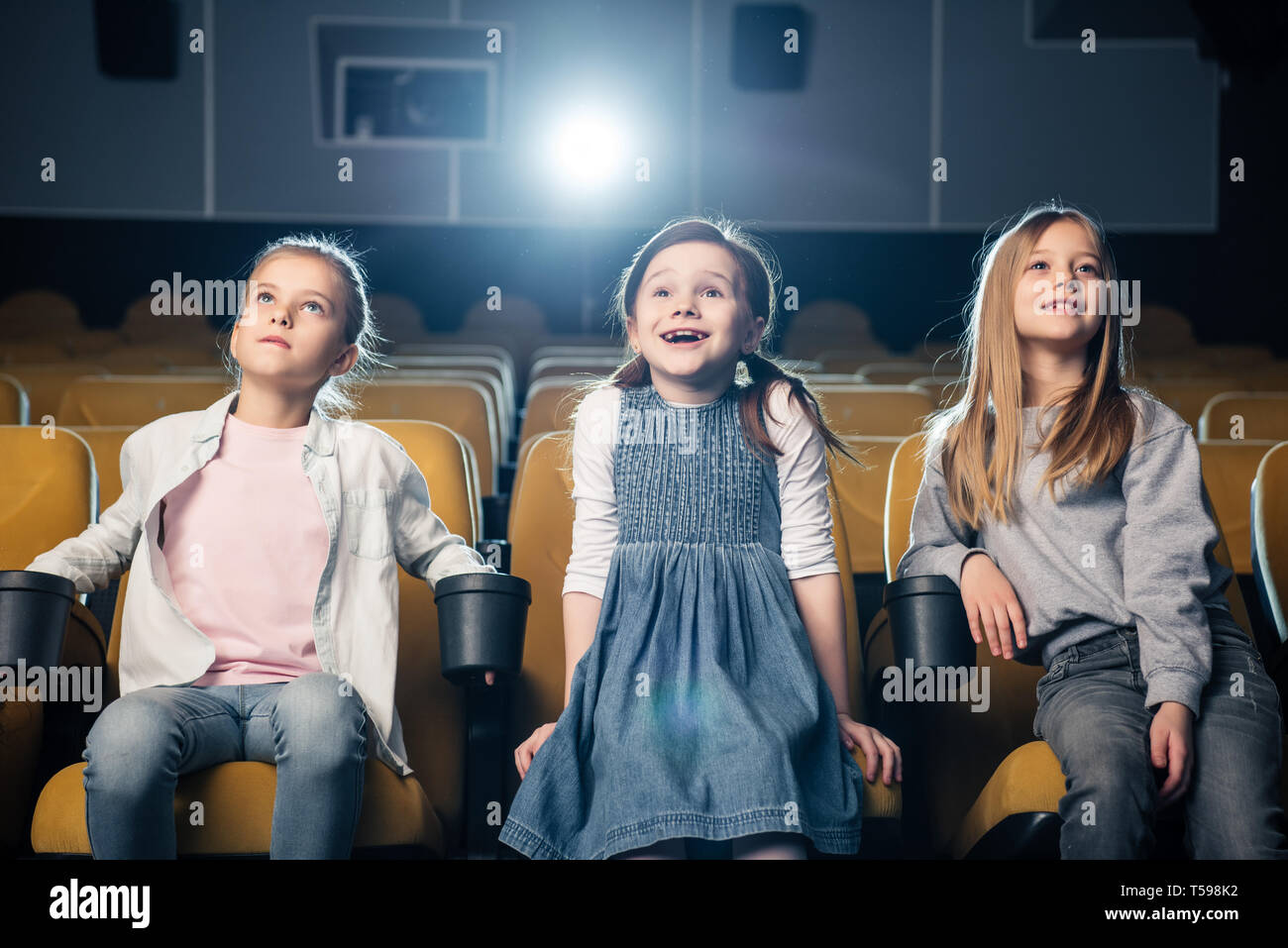 three adorable smiling kids watching movie in cinema together Stock