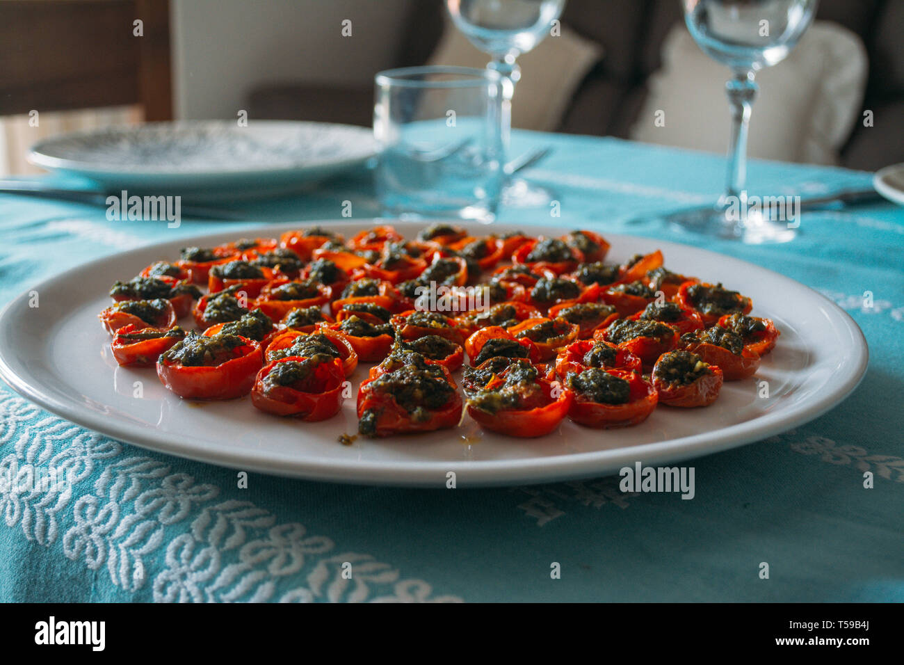 cherry tomatoes cooked with green sauce on a white dish on turquoise tablecloth Stock Photo
