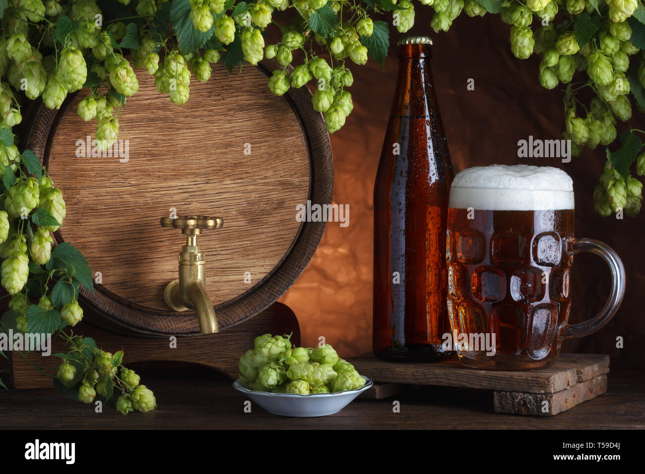 Bottled and unbottled beer with barrel and fresh hops for brewing still