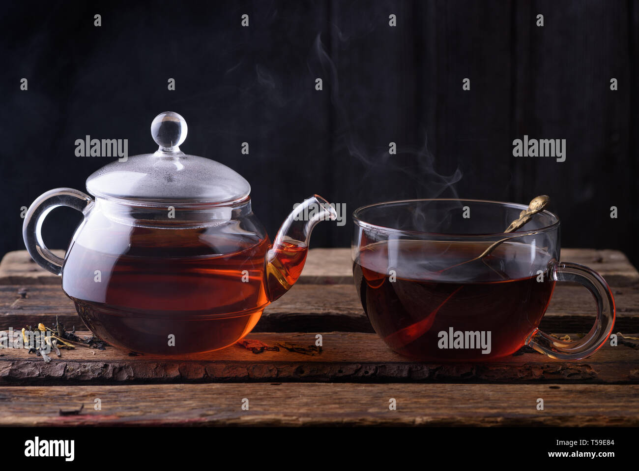 https://c8.alamy.com/comp/T59E84/hot-tea-in-glass-teapot-and-cup-with-spoon-and-steam-on-wooden-table-dark-still-life-T59E84.jpg