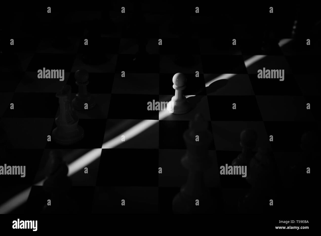 black and white photo of a pawn isolated in the center of the board with a ray of light Stock Photo