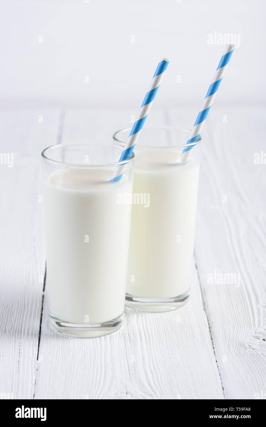 Two glasses of milk with blue stripped paper straw on white wooden table still life Stock Photo