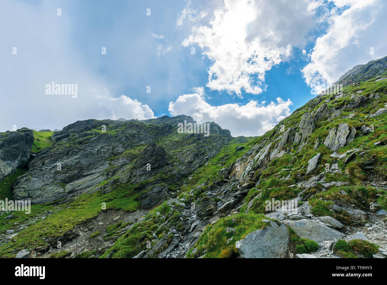 hiking uphill rocky slopes of fagaras mountains. hard path among big and sharp boulders. sunny summer weather with cloudy sky Stock Photo