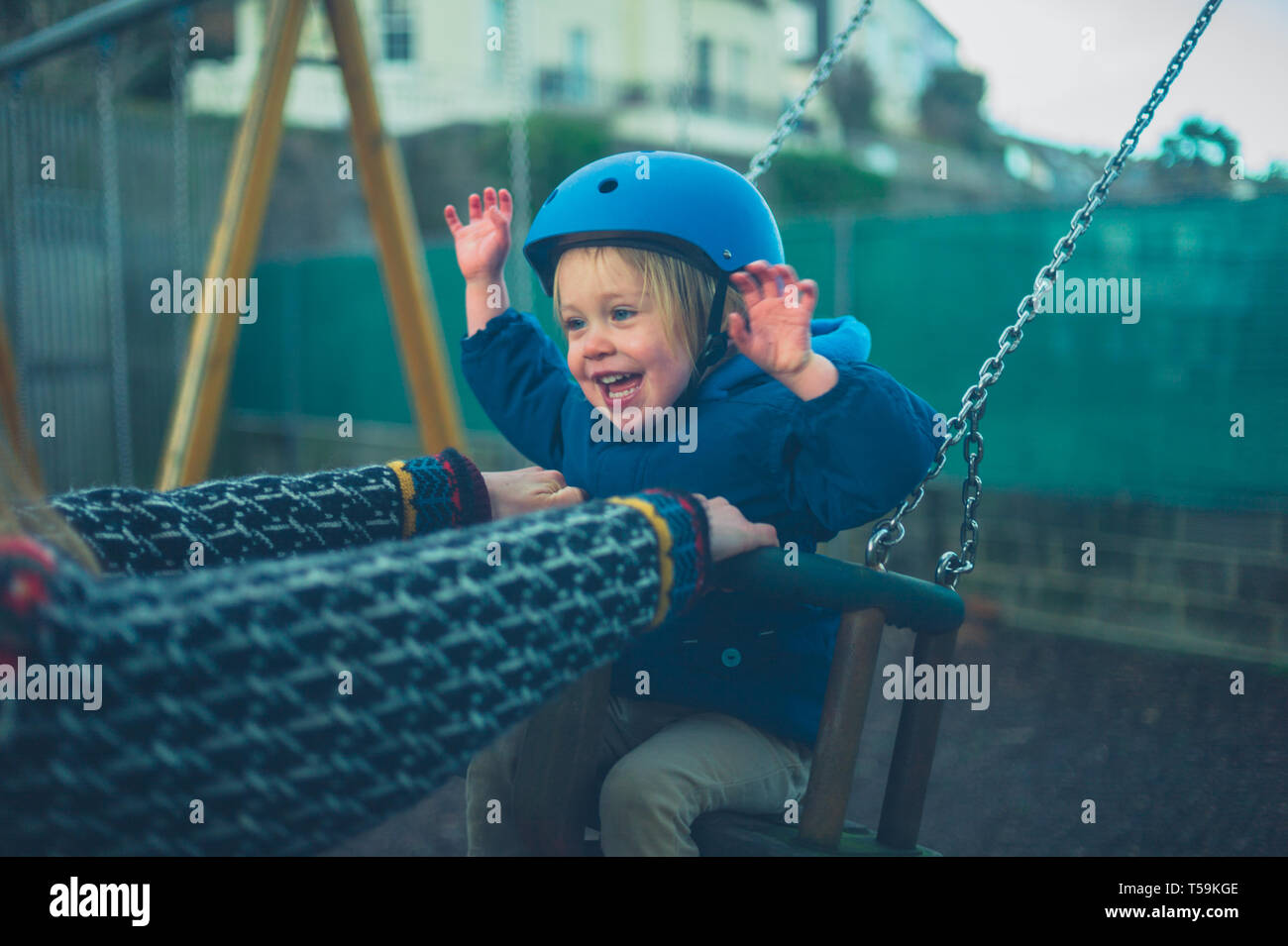 A little toddler wearing a helmet is on the swing in the playground Stock Photo