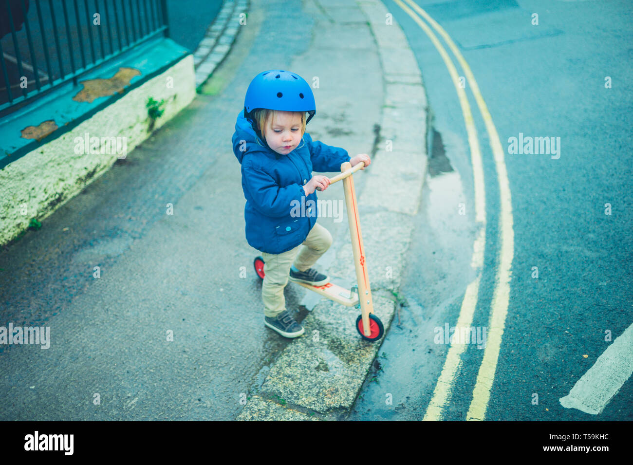 A little toddler wearing a helmet is riding a scooter in the street