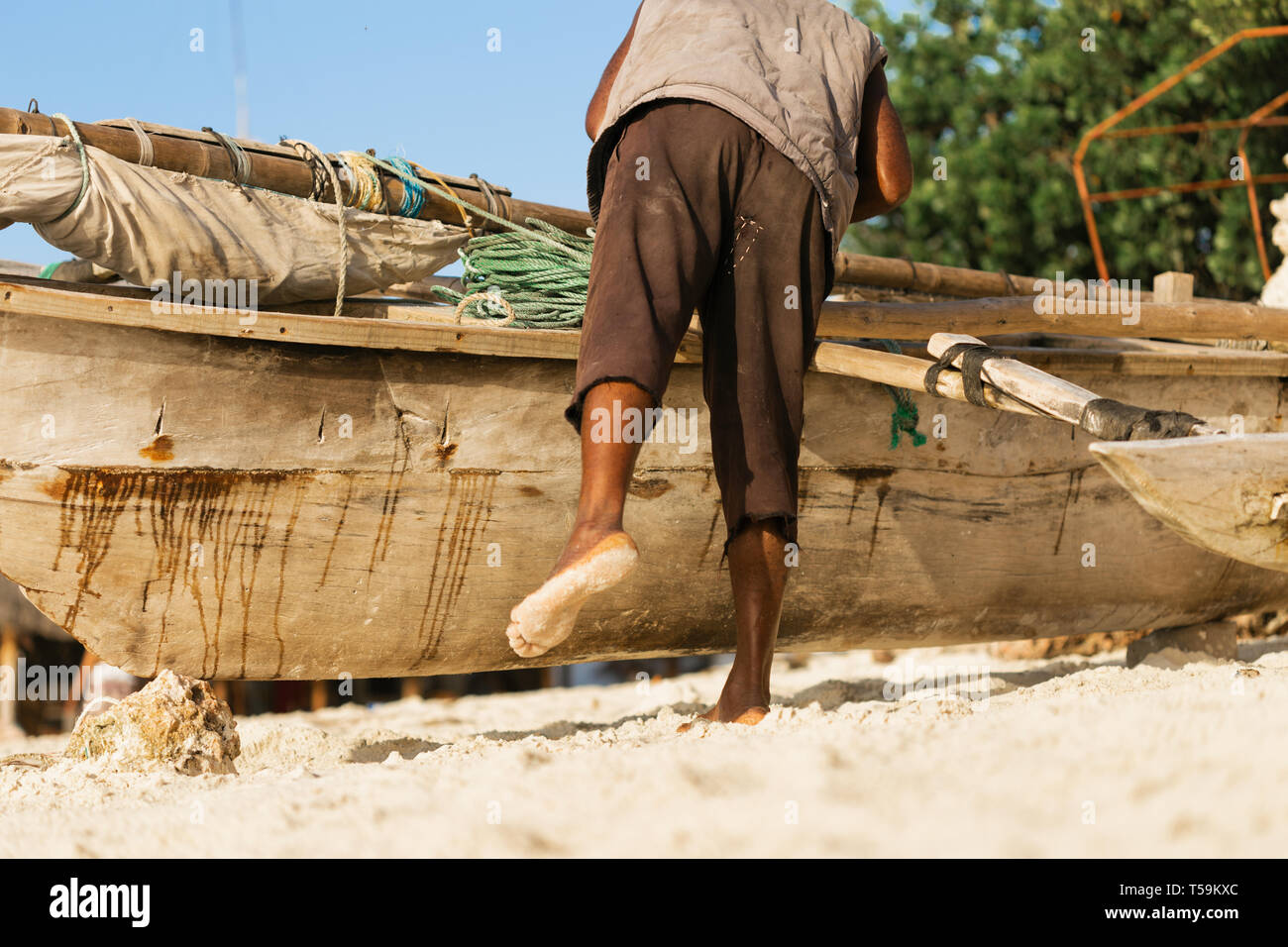 Poor African fisherman repairing his old wooden boat on the ocean Stock Photo