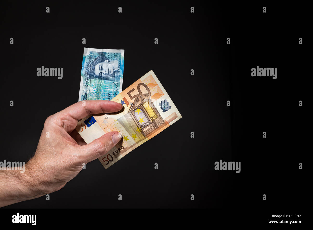 A male hand holding a five pound and 50 (fifty) Euros banknotes, brexit concept, isolated over black. Stock Photo