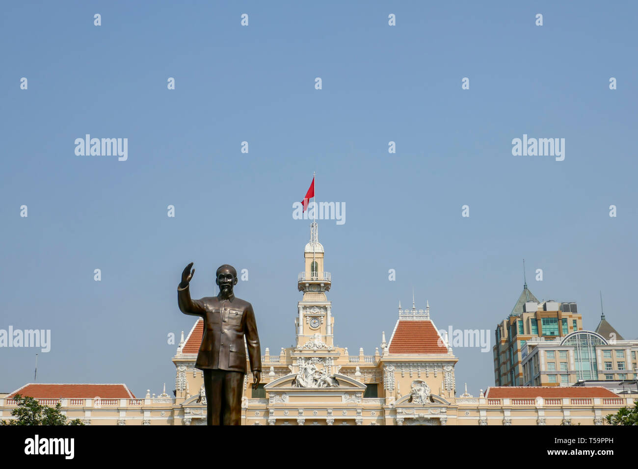 Statue of Ho Chi Mnh, or Uncle Ho, in front of City Hall with Vietnmese flag against blue skies with copy space in Ho Chi  Minh City, Vietnam. Stock Photo