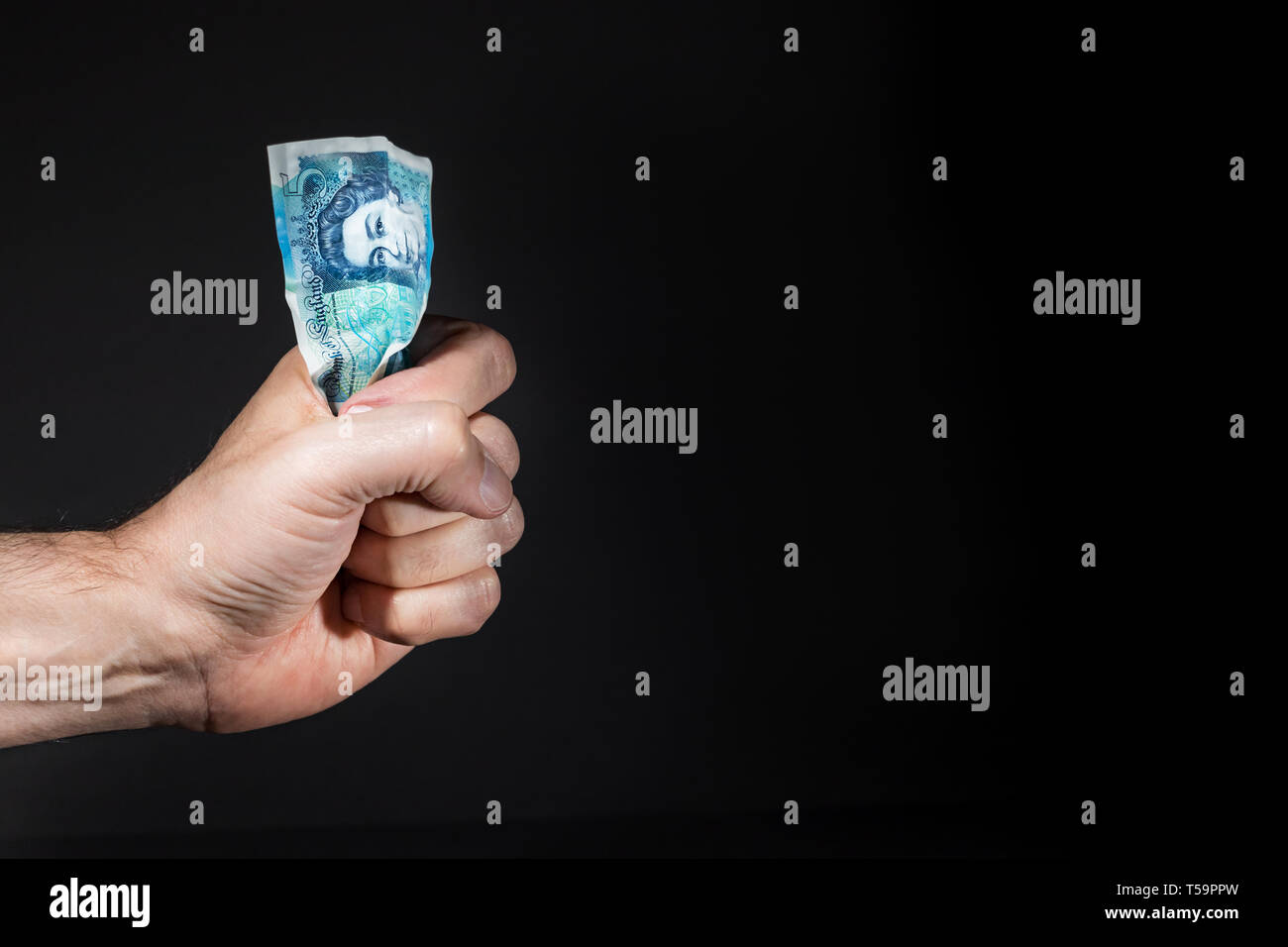 A male hand holding a five pounds banknote on his fist, isolated over black. Stock Photo