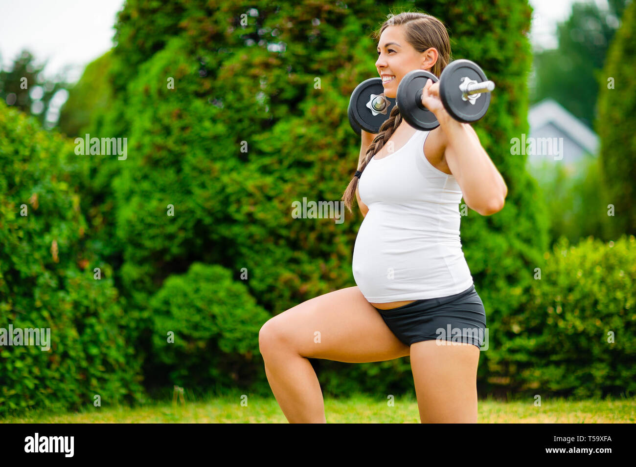Pregnant Woman Doing Kneeling Lunges With Dumbbells In Park Stock Photo