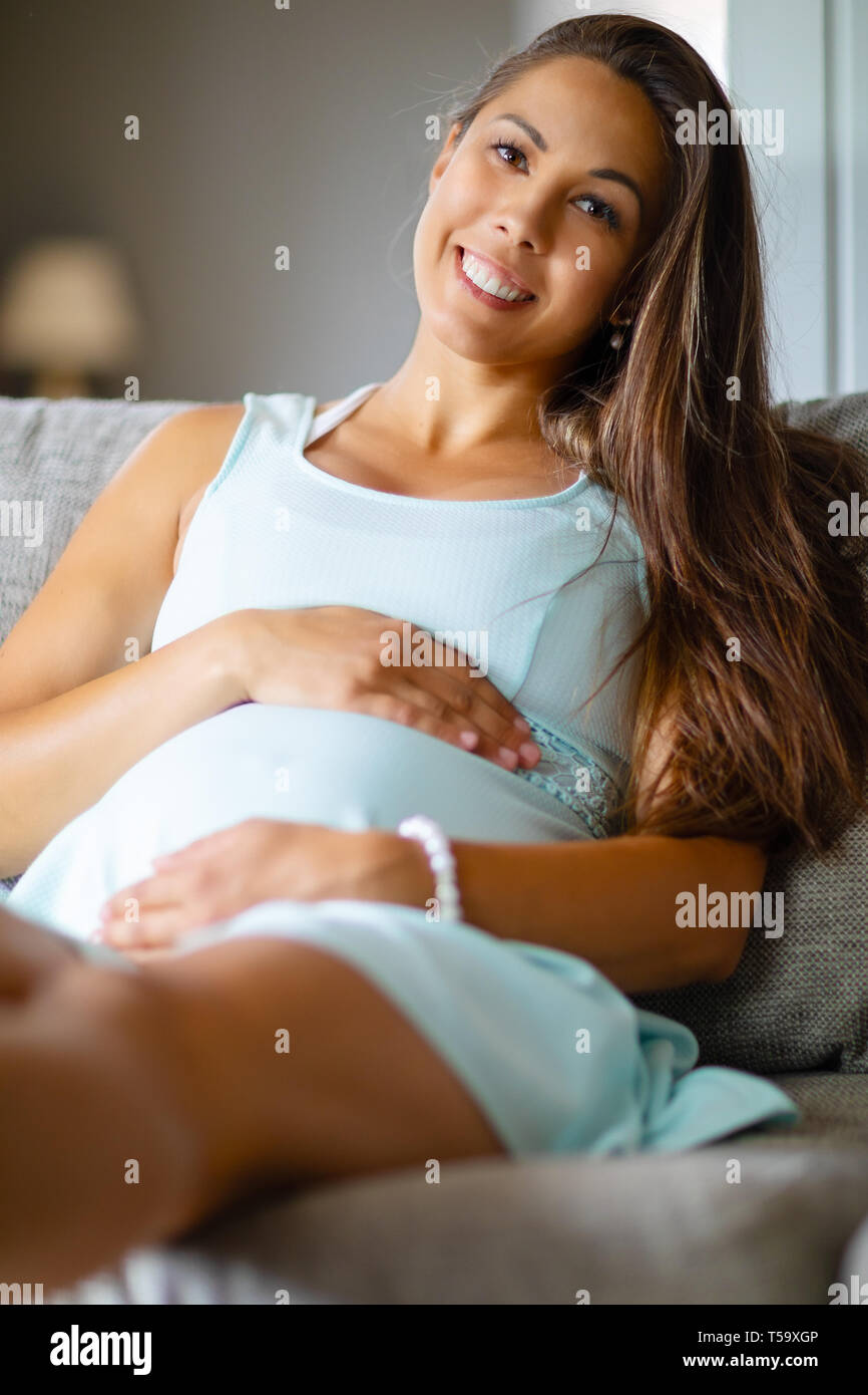 Positive pregnant woman in dress on the sofa holding on belly Stock Photo